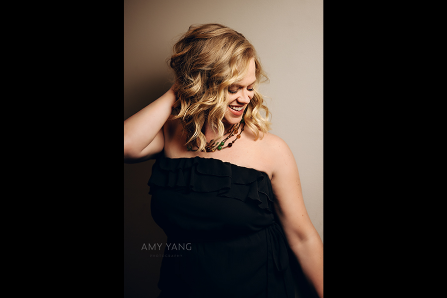 headshot of woman wearing a black dress with her hand in her hair