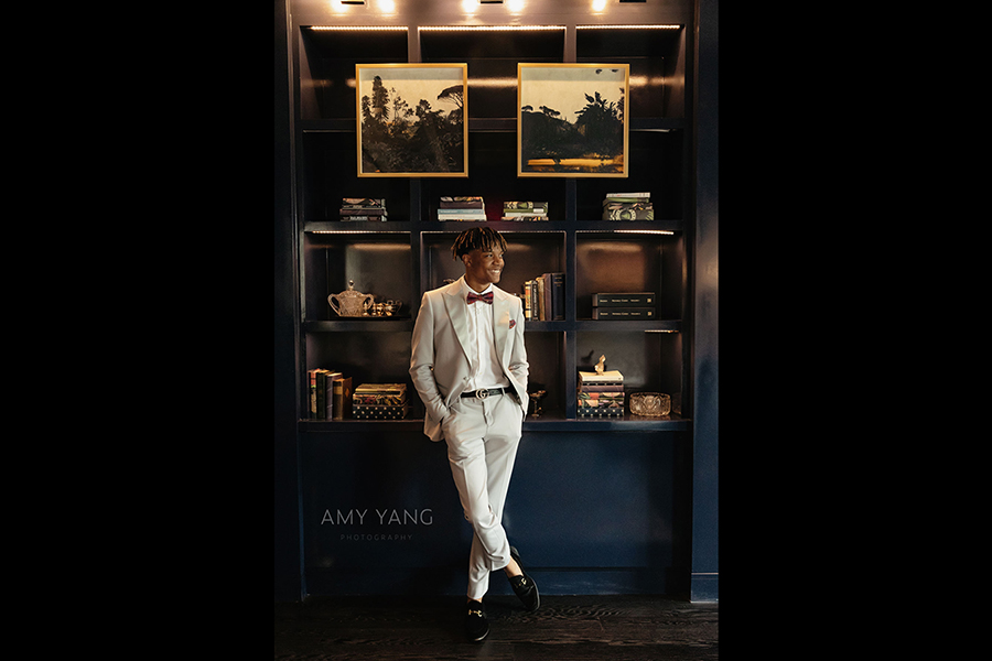 headshot of a man in a white suit with a Gucci belt standing in library