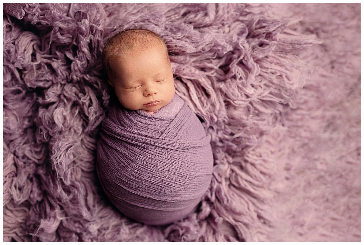 baby swaddled in purple sleeps on purple rug by Amy Yang Photography