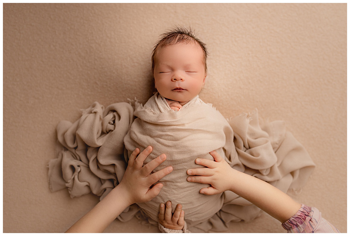 siblings place hand on swaddled baby during family newborn studio session