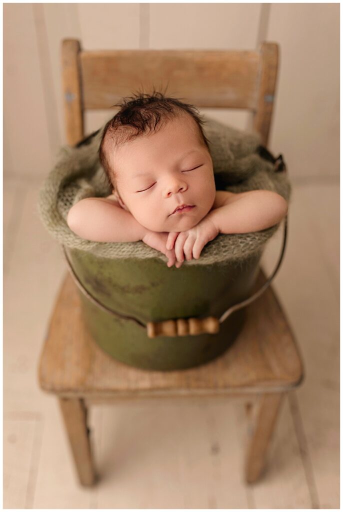 infant rests head on hands in a bucket during family newborn studio session