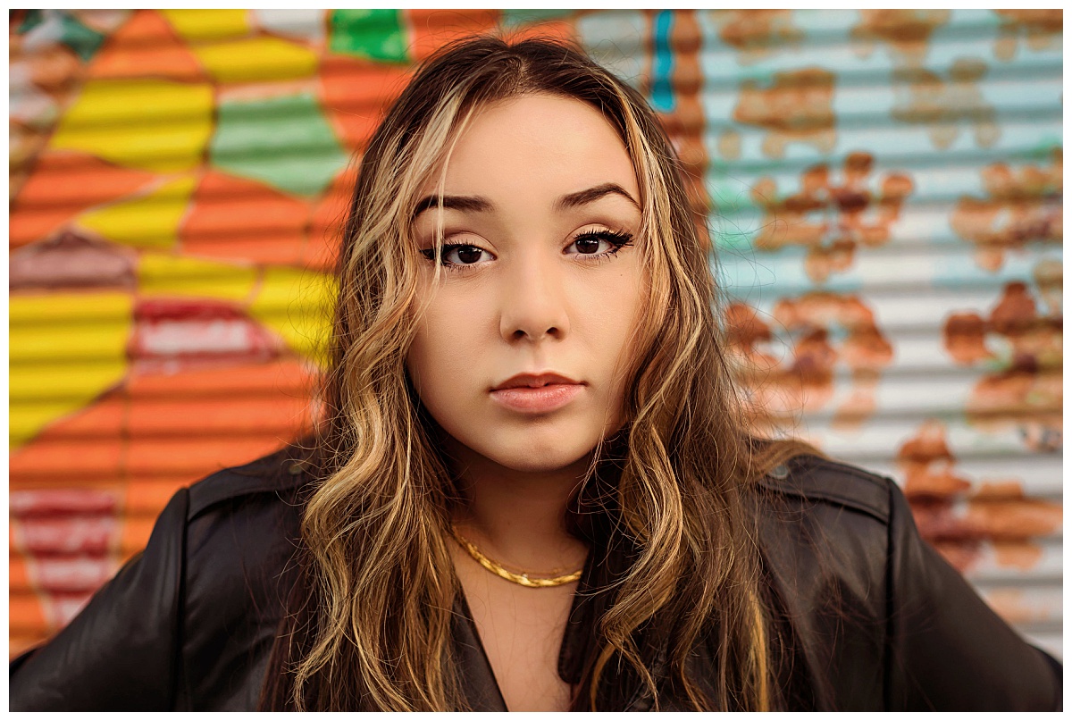 high school student looks straight ahead in front of colorful wall by Amy Yang Photography