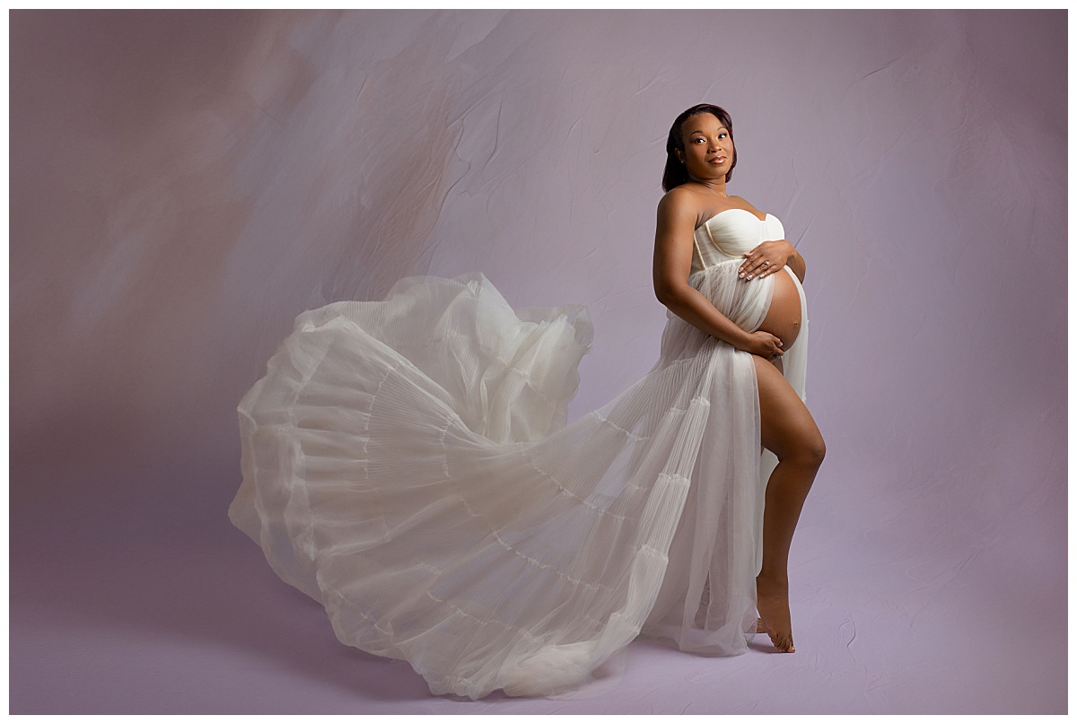 mother holds pregnant belly as skirt flows out from her by Charlottesville photographer