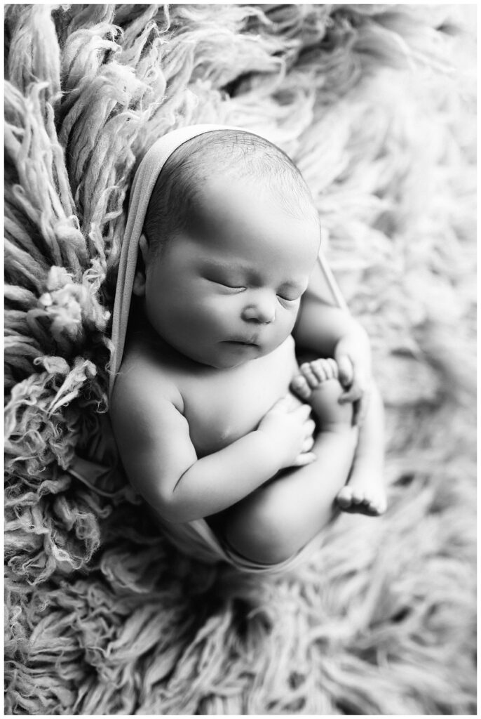 little one holds foot while swaddled by Charlottesville newborn photographer