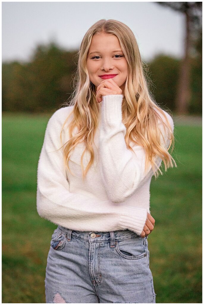 blonde in a white sweater rests her hand on her chin and smiles by Amy Yang Photography