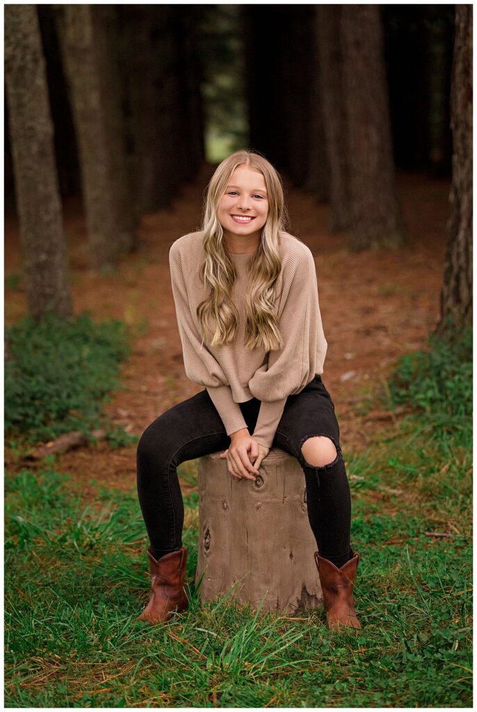 blonde leans forward while sitting on stump by Amy Yang Photography