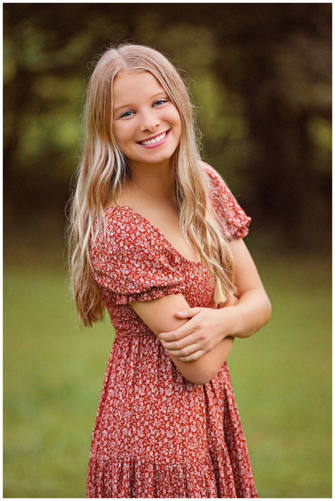 high school student folds arms and leans forward as she smiles by Charlottesville luxury photographer